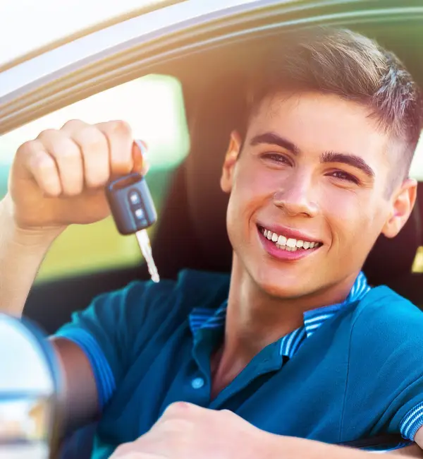 A young man beams with joy as he leans out of his car window, holding up the keys to his brand-new vehicle Auto Insurance